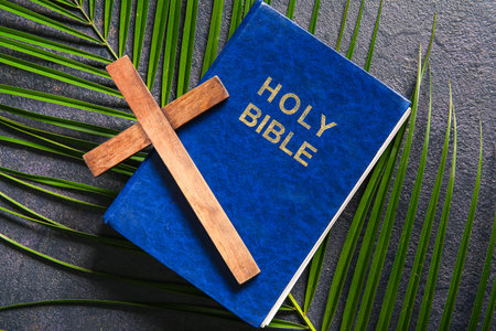 Wooden cross with palm leaf and Holy Bible on black background