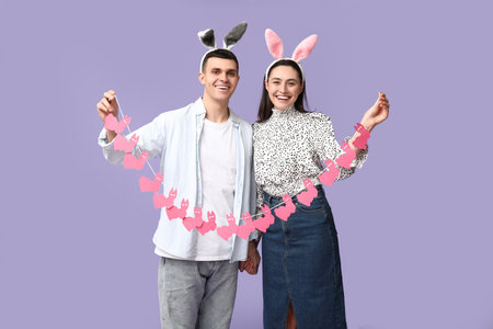 Happy young couple with Easter garland and bunny ears on lilac background