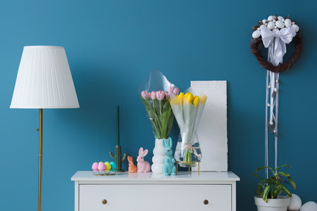 Vases with tulips, Easter rabbits and eggs on commode in roomの写真素材
