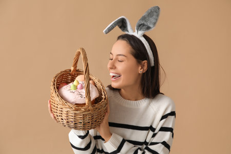 Pretty young woman with bunny ears and Easter basket on beige backgroundの写真素材