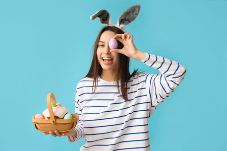 Pretty young woman with bunny ears and Easter basket on blue background
