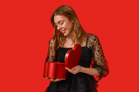 Young woman opening gift box on red background. Valentine's Day celebration