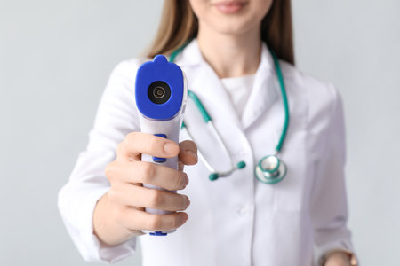 Female doctor with infrared thermometer on light background, closeupの写真素材