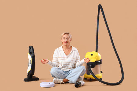Mature woman with vacuum cleaners meditating on beige backgroundの写真素材