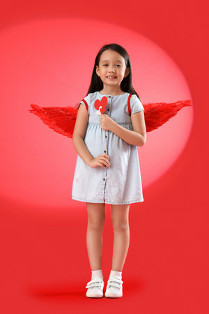 Cute little Asian girl with Cupid's wings and hearts on red background. Valentine's Day celebration