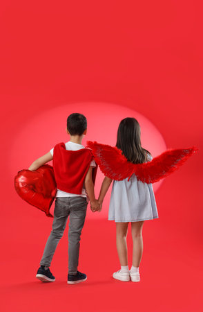 Cute little children with balloon holding hands on red background, back view. Valentine's Day celebrationの写真素材