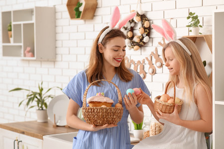 Cute little girl and her mother in bunny ears holding baskets of Easter cake with painted eggs in kitchenの写真素材