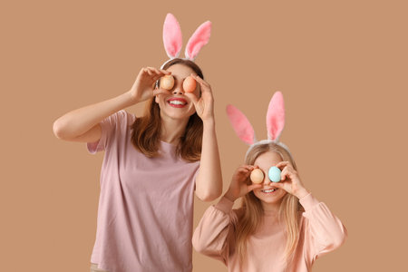 Cute little girl and her mother in bunny ears with painted Easter eggs on brown background