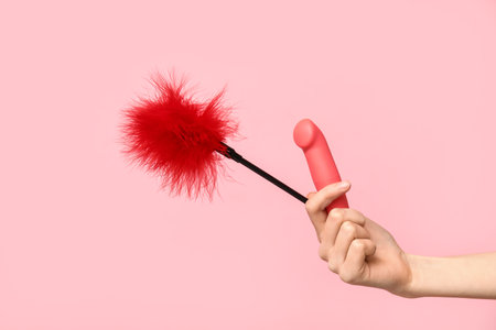 Female hand with vibrator and feather stick from sex shop on pink backgroundの写真素材