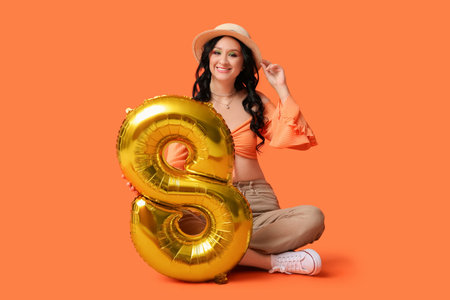 Beautiful young woman with golden air balloon in shape of figure 8 on orange background....