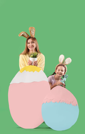 Cute little girl with her mother in bunny ears and Easter decor on green background