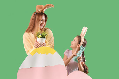 Cute little girl with her mother in bunny ears and Easter decor on green background