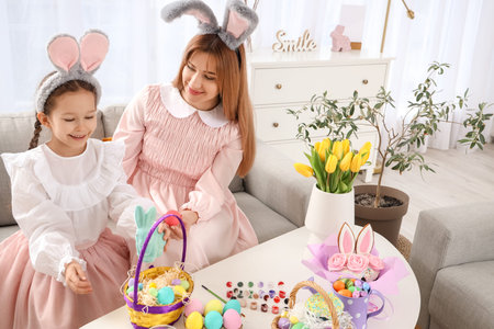 Cute little girl with her mother in bunny ears and Easter basket on table at home
