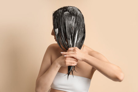 Young woman applying hair mask on beige background, closeupの写真素材