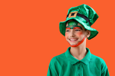 Funny boy with face painting and leprechaun's hat on orange background. St. Patrick's Day celebrationの写真素材