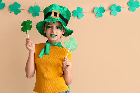 Funny girl with face painting, leprechaun's hat and clovers near beige wall. St. Patrick's Day celebrationの写真素材