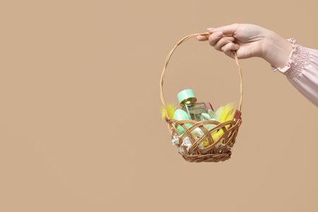 Female hand with wicker basket full of Easter eggs and decorative cosmetics on brown backgroundの写真素材