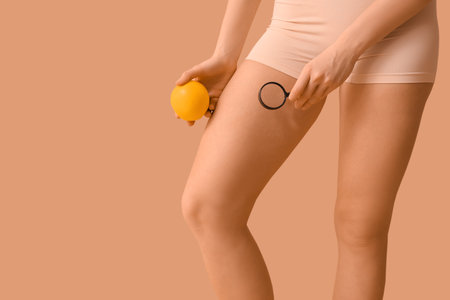 Beautiful young woman with cellulite problem, magnifier and orange on brown backgroundの写真素材