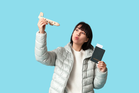 Beautiful young woman with wooden airplane, passport and ticket on blue background. Winter vacation...