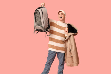 Handsome young happy man with backpack and jacket on pink background. Winter vacation concept