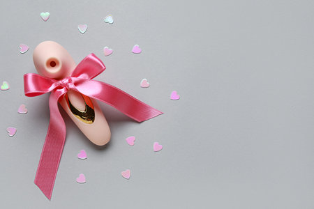 Vibrator with bow and confetti on gray background. Valentine's Day celebration