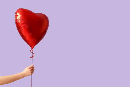 Woman with air balloon in shape of heart on lilac background. Valentine's Day celebrationの写真素材