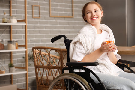 Young redhead woman in wheelchair with cup of tea at homeの写真素材