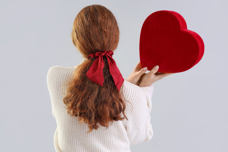 Young redhead woman with ponytail and scrunchy holding heart on light background, back viewの写真素材