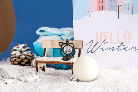Beautiful composition with greeting card and different Christmas decorations on snow against blue...