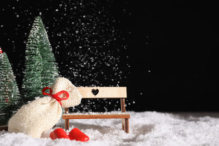 Beautiful composition with bench, Christmas fir trees and decorations on snow against black backgroundの写真素材