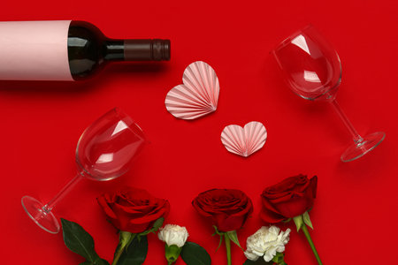 Bottle of wine with beautiful flowers and glasses on red background. Valentine's Day celebrationの写真素材