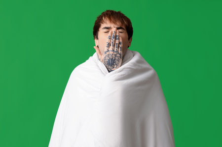 Sleepy young man with blanket yawning on green backgroundの写真素材