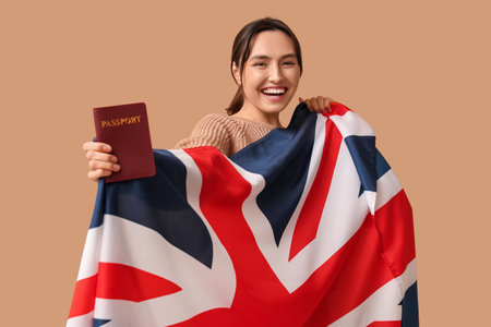 Pretty young woman with UK flag and passport on beige background. Immigration conceptの写真素材
