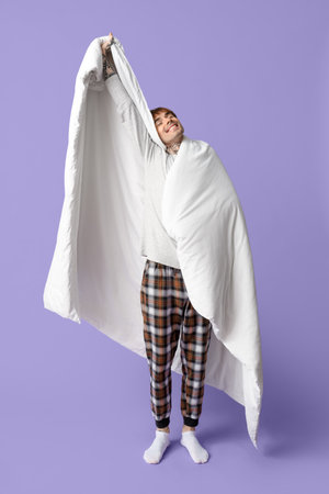 Handsome young man with blanket stretching on lilac backgroundの写真素材
