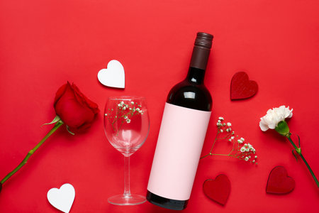 Bottle of wine with glass, flowers and hearts on red background. Valentine's Day celebrationの写真素材