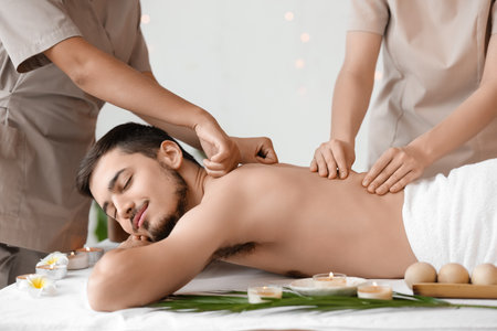 Young man getting massage from therapists in spa salonの写真素材