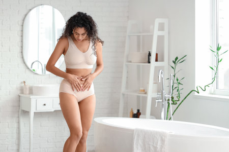 Young African-American woman wearing beige menstrual panties in bathroomの写真素材