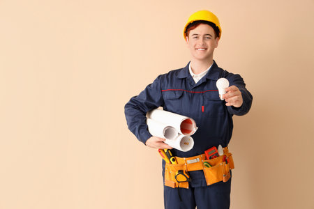 Male electrician with light bulb and house plans on beige backgroundの写真素材