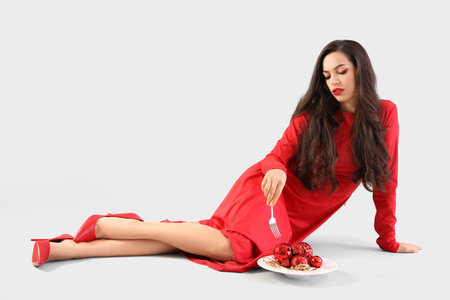 Beautiful young woman with plate of Christmas balls sitting on gray backgroundの写真素材