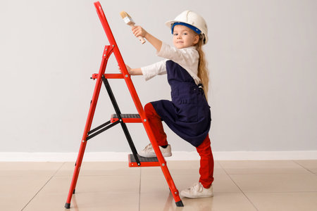 Cute little decorator with brush and stepladder near light wall. Opposite Day celebrationの写真素材