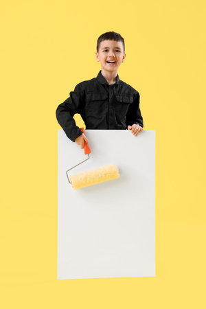 Cute little decorator with paint roller and blank poster on yellow background. Opposite Day celebrationの写真素材