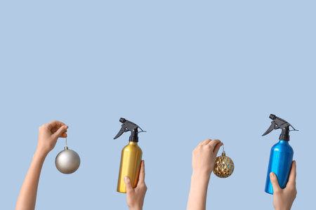 Hands holding hair spray and Christmas decorations on light blue background