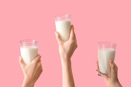 Hands with glasses of milk on pink backgroundの写真素材