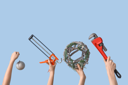 Hands holding construction tools and Christmas decorations on light blue backgroundの写真素材