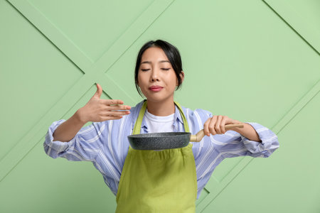 Portrait of young Asian woman with frying pan on green backgroundの写真素材