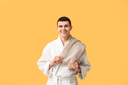 Portrait of handsome young man in bathrobe and towel on yellow backgroundの写真素材