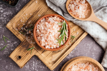 Wooden spoon and bowl of Himalayan pink salt with rosemary on dark backgroundの写真素材