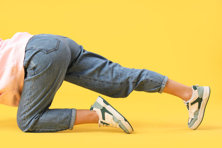 Young woman in trendy jeans on yellow background