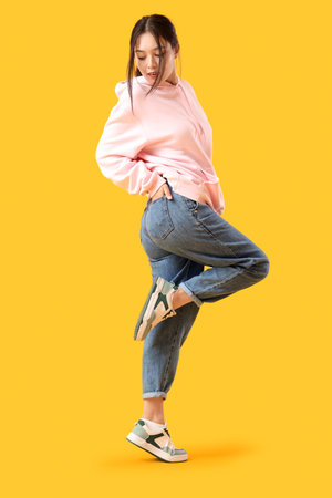 Young Asian woman in trendy jeans on yellow backgroundの写真素材