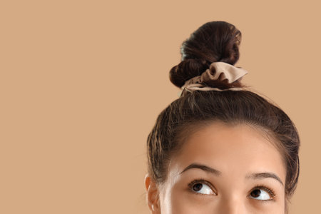 Young Asian woman with bun and scrunchy on beige background, closeupの写真素材